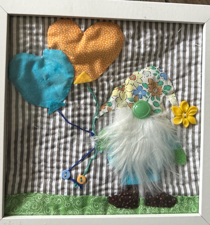 Whimsical quilted gnome with teal and orange heart balloons on gray gingham background in white frame