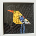 Geometric patchwork bird quilted appliqué wall art with green button eye on dark charcoal background in white frame