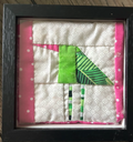 Framed quilted green bird wall art with lime green and pink fabric on white background in black frame