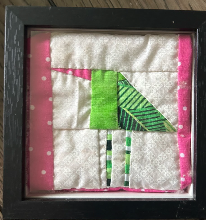 Framed quilted green bird wall art with lime green and pink fabric on white background in black frame