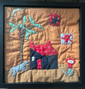 Framed folk art quilted wall art with house, palm tree, dog, cat and red flowers on golden background in black frame