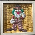Cheerful quilted clown appliqué wall art with button eyes on golden yellow background in natural wood frame