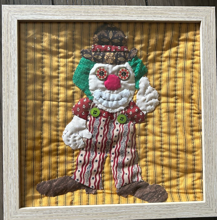 Cheerful quilted clown appliqué wall art with button eyes on golden yellow background in natural wood frame